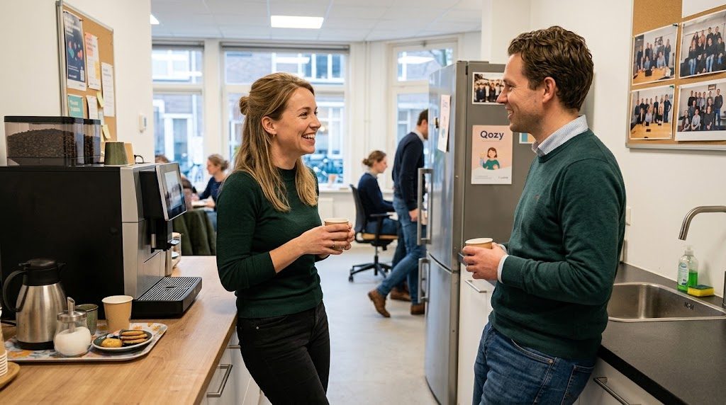 Een vrouw en een man staan lachend met een kop koffie te praten in een keuken op kantoor.